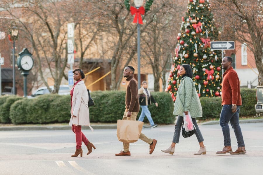 Two Couples walking across River Street downtown with shopping bags and a Christmas tree in the background